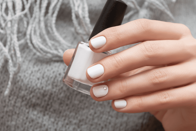 A woman with white nails holding white nail polish